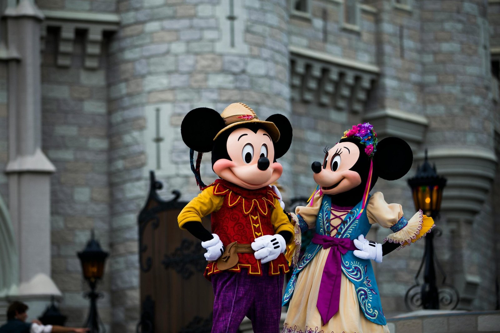 Mickey and Minnie Mouse in colorful costumes outside an iconic castle setting.